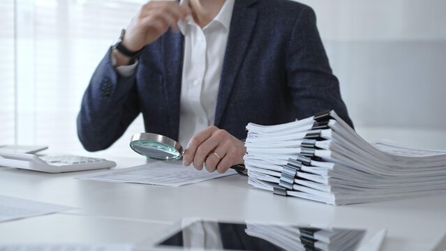 Professional accountant or auditor carefully examining financial documents and corporate reports with a magnifying glass, diligently researching tax obligations and legal compliance. Audit and taxes