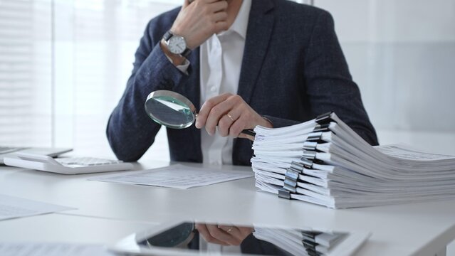 Professional accountant or auditor carefully examining financial documents and corporate reports with a magnifying glass, diligently researching tax obligations and legal compliance. Audit and taxes