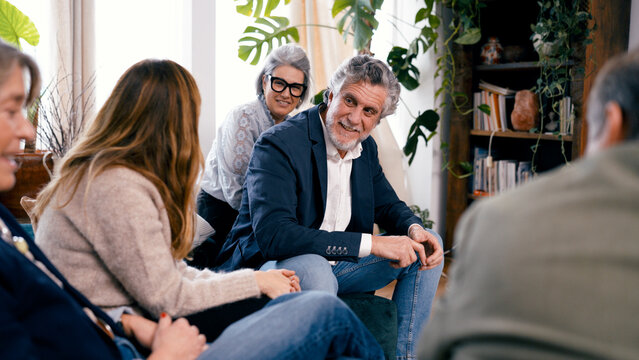 Group of seniors friends sitting indoors, having a social gathering and smiling while engaging in joyful conversation