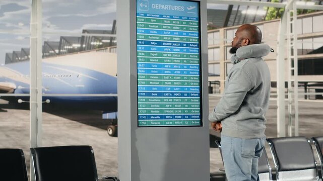 Checking departure board, timetable data and African american man in airport lounge. Catching plane, flight status information on display and multiracial travelers doing holiday trips