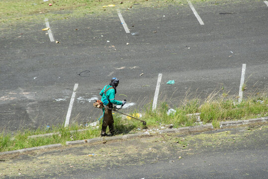 A city hall employee is seen mowing tall grass in the Sao Raimundo parking lot. Salvador, Bahia.