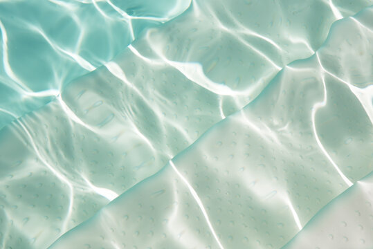 Crystal clear turquoise swimming pool water surface with natural light reflections and gentle ripples. Perfect summer background for wellness, spa, travel, luxury lifestyle and minimalist design uses.