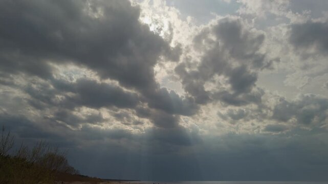 Soft light over ocean with gathering storm clouds, muted tones and diffuse rays creating contemplative atmosphere, distant sea meeting heavy layered sky above empty shore