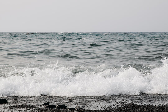 A seething wave crashes onto the shore on a black volcanic beach.