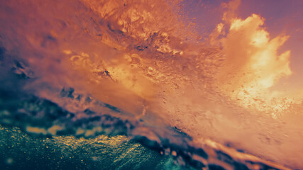 Obraz premium Underwater view of a breaking ocean wave with golden sunset light reflecting through the water surface and dynamic textures.