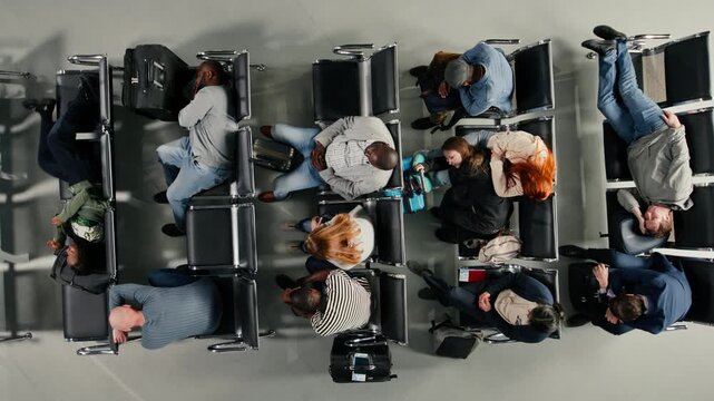 Top down view of tired passengers sleeping in airport during air transport blockage causing delayed flights. Tourists napping on chairs in lounge, waiting for another airplane, high angle shot
