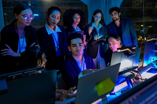 Friendly senior East Asian employee smiling genuinely while working late at night in a dimly lit office. Mature man at his desk