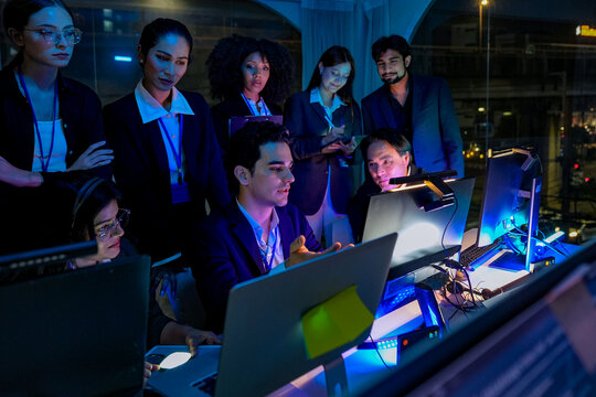 Friendly senior East Asian employee smiling genuinely while working late at night in a dimly lit office. Mature man at his desk