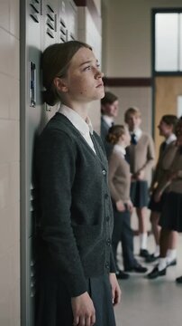 Young woman leaning against grey school locker in hallway with students in background medium shot