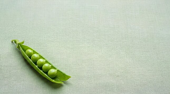 Single fresh green pea pod split open to show peas inside, resting in the lower left corner of a large light green linen surface, most of the linen kept empty as negative space.
