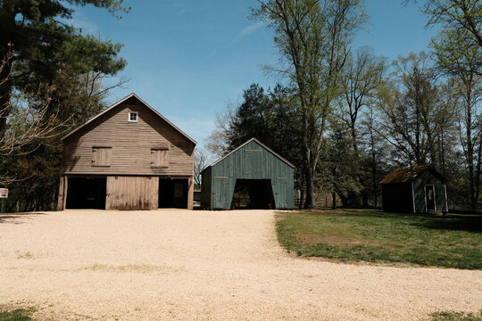 A collection of weathered wooden barns and outbuildings in a rural farm landscape with a gravel path