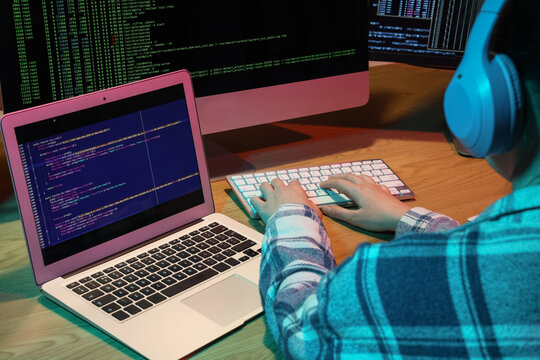 Female programmer with headphones working in office at night, back view