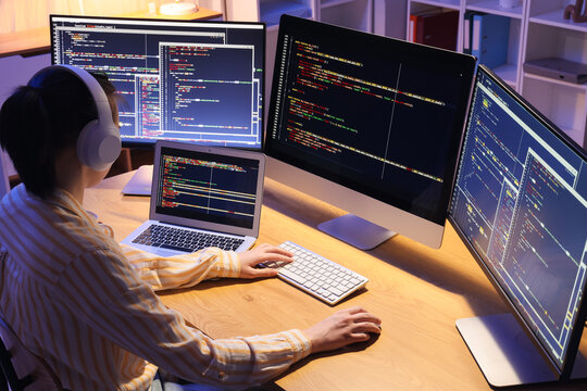 Female programmer with headphones working in office at night, back view