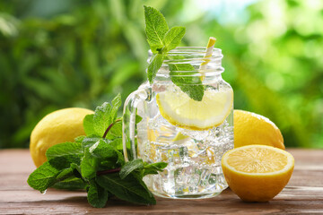 Obraz premium Lemon water in mason jar, mint and citrus fruits on wooden table against blurred background, closeup