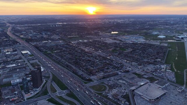 Cinematic aerial drone pull-back from Yorkdale Shopping Centre, revealing the heavy evening traffic on Highway 401 and the vast urban sprawl of North York against a vibrant sunset