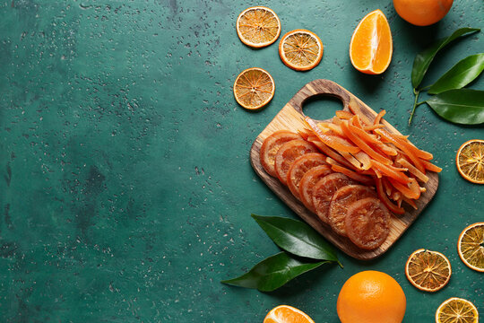Wooden board with tasty candied orange peels and slices on green grunge background