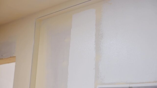 Person painting wall with brush roller near ceiling. Interior renovation and home improvement process