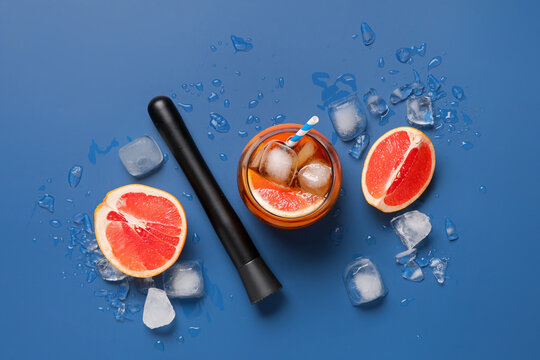 Glasses of cold tea with grapefruit slices and muddler on blue background