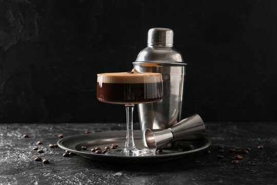 Glass of tasty espresso martini cocktail, jigger and shaker on black grunge background, closeup