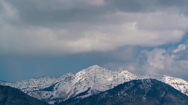 Time lapse of clouds moving over snow-capped mountains in Utah during spring.