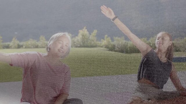 Two women doing fitness outside mature woman lifting arm teen mirroring wearing wrist bands on mats