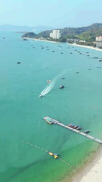 Sanya, Hainan - May 3 2026: A boat pulls a colorful parasail over the bright blue water of Yalong Bay with luxury resort hotels in the background