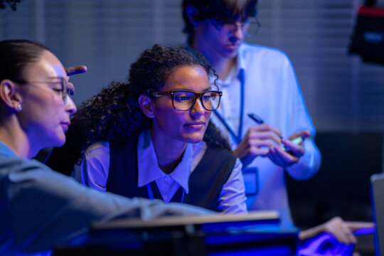 young professionals discussing business strategy and reviewing data on laptop in a creative. Business specialists analyzing digital data a high tech corporate office at night. Strategic collaboration.