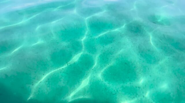 Calm turquoise sea surface with soft light reflections forming natural patterns seen from boat in clear shallow water