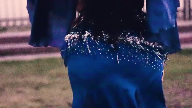 A glimpse of the hips and legs of a beautiful Latina woman dancing belly dance, moving her thighs and the jewels of her blue dress with sensuality and joy.