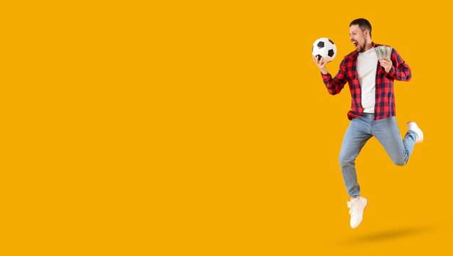Happy young man with soccer ball and money jumping on yellow background with space for text. Sports bet concept