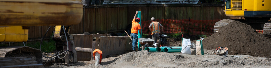 Fototapeta premium Stormwater system pipe installation in progress, construction workers with 6 in green PVC pipes standing above excavated dirt trench on infrastructure work site 