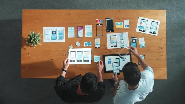 Software developer team holding software icon and discussing about Ux Ui design for mobile phone interface. Top view of programmer work together to brainstorm wireframe prototype design. Convocation.