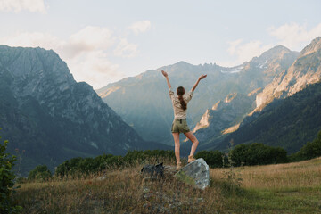 Young woman with backpack stands on rock in mountain valley raises arms enjoys nature and freedom during hiking adventure in scenic landscape outdoors. © SHOTPRIME STUDIO