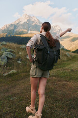 Fototapeta premium A woman hiker with a backpack stands on a grassy trail, gazing toward distant mountains. The scene conveys exploration, freedom, and the allure of outdoor adventure.