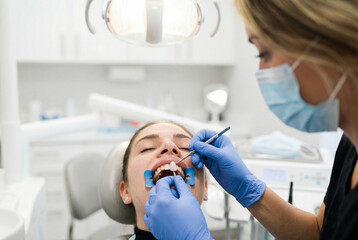 Fototapeta premium Dentist wearing blue gloves examining the teeth of a female patient in a clinic