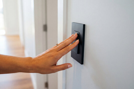 Woman hand pressing a modern black light switch on a white wall