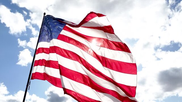 Patriotic US Flag Waving Against Blue Sky and Sunlit Clouds