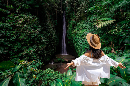Solo female traveler with outstretched arms, enjoying freedom and peace in a lush tropical rainforest at Leke Leke waterfall in Bali, Indonesia