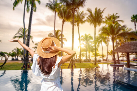 Female traveler relaxing by a luxurious tropical swimming pool surrounded by palm trees at golden hour, summer vacation