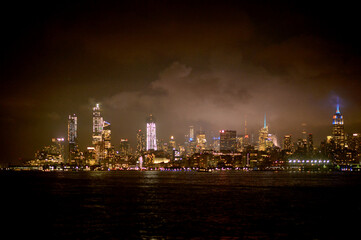 Fototapeta premium City Lights Flicker Over River. Soft Illuminated Skyline Reflects Calm Nocturnal City Atmosphere