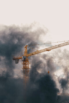 Construction crane in dense dark smoke from fire. Urban catastrophe and emergency situation idea