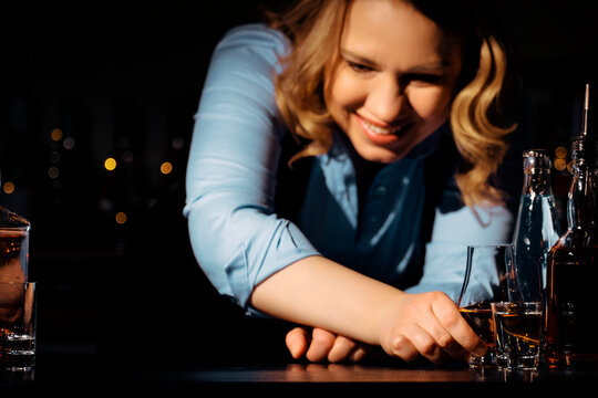 Smiling woman sommelier serving strong alcohol drinks at bar counter. Friendly professional hospitality and service.