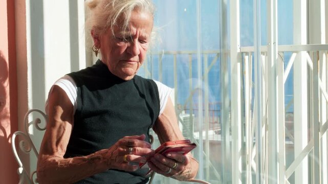 active senior woman using a smartphone by a bright window. Concept of silver economy, digital literacy for elderly, and staying connected in retirement