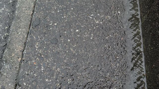 Rainwater Runoff Along Wet Asphalt Edge with Rough Pavement Texture