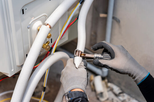 Technician hands in gloves using pipe cutter on insulated copper tubing for air conditioner, HVAC worker installing copper pipes with insulation for outdoor condensing unit