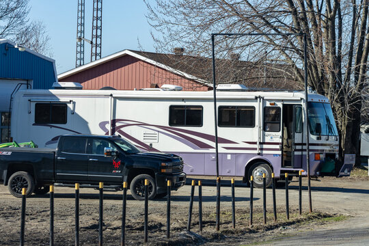 Quebec, Canada, 24 April 2026 : A large recreational vehicle and a Chevrolet Silverado pickup truck are parked outdoors near buildings.