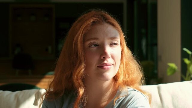 A beautiful young redhead woman with freckles is captured in a serene moment of relaxation and contemplation. Her peaceful expression conveys a sense of calm and well-being as sunlight bathes her fa