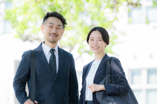 新緑の中屋外のビルの前で笑顔のビジネス男女のポートレート　上司や信頼とキャリアイメージカメラ目線笑顔
