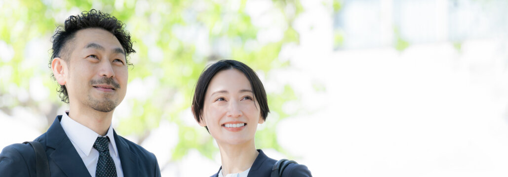 新緑の中屋外のビルの前で笑顔のビジネス男女のポートレート　上司や信頼とキャリアイメージ未来や希望で見上げる、見つめる笑顔	バナー