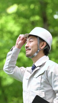 公園などでヘルメット姿でタブレットで点検する林業や施工管理などの現場作業員のポートレート安全管理とDX業務　カメラ目線上半身クローズアップ動画